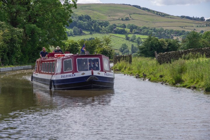 Narrowboat on a canal with green hills in the background.
