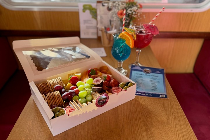 Food box with crackers, fruits and drinks on a table inside a cozy setting.