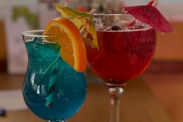 Two colorful cocktails with umbrellas on a wooden table.