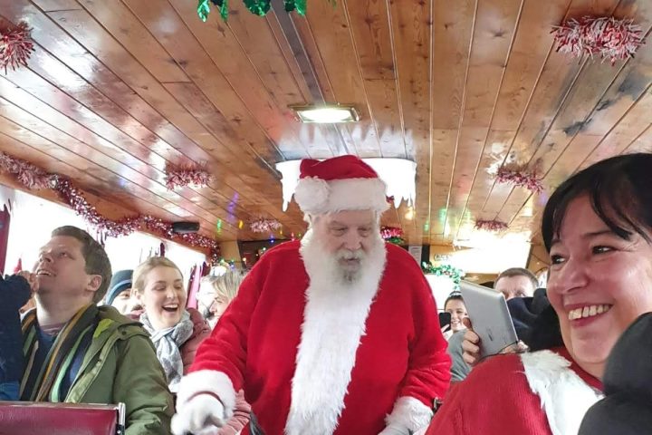 Santa Claus walking down a crowded train aisle with festive decorations.