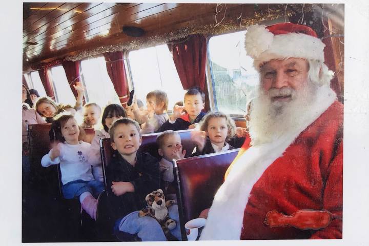 Santa with children on a holiday-themed bus, smiling and waving.