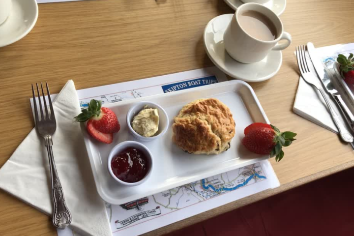 Cream tea setup with scone, jam, cream, strawberries, and tea on a tray.