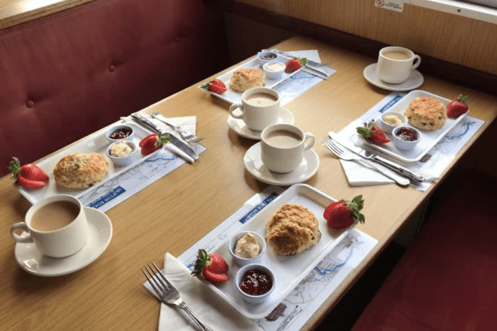 Table set with scones, jam, cream, strawberries, and tea on plates and mugs.