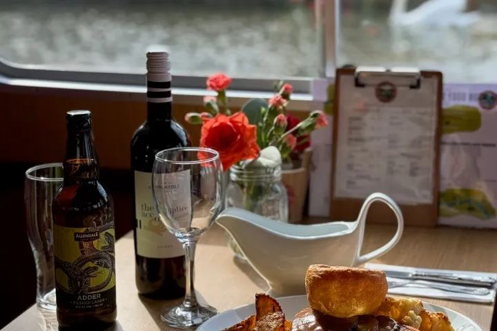 Table with roast dinner, wine bottle, beer, and swan visible through window.