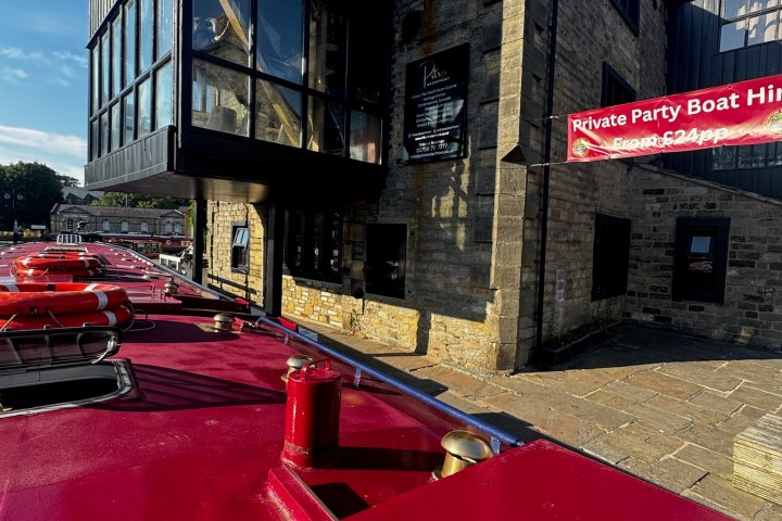 Red canal boats docked beside a stone building under a clear blue sky.