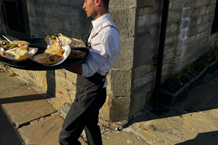 Waiter carrying trays with food outside in sunlight.
