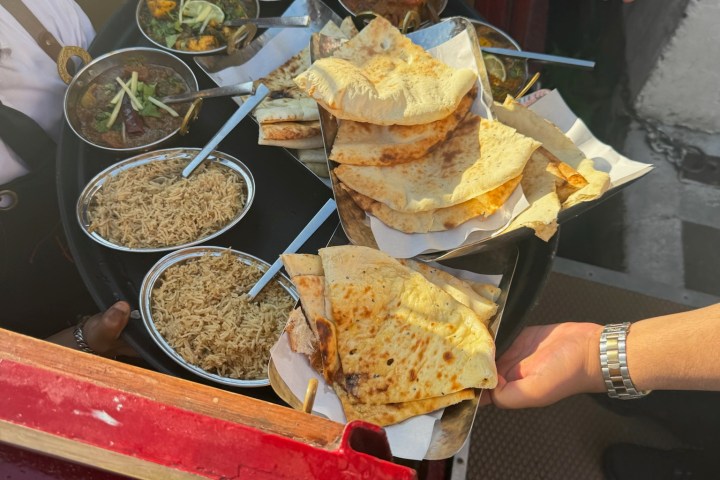 Hand reaching for tray of naan bread on a table with bowls of rice and curry dishes.