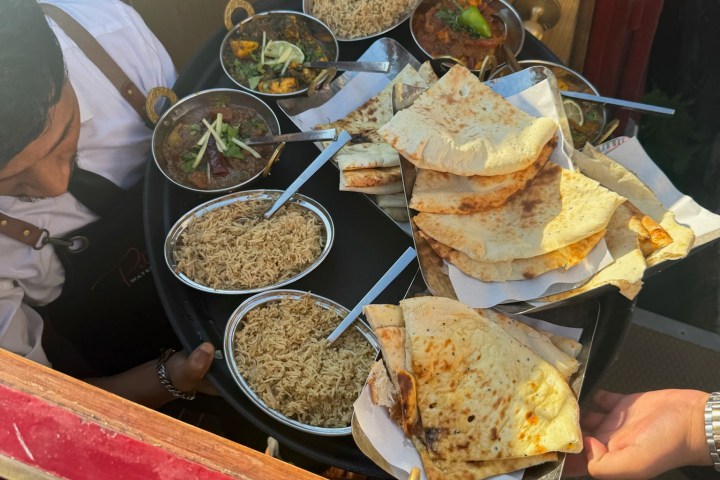 Tray with naan, rice, and curry dishes being served by a person on a train.