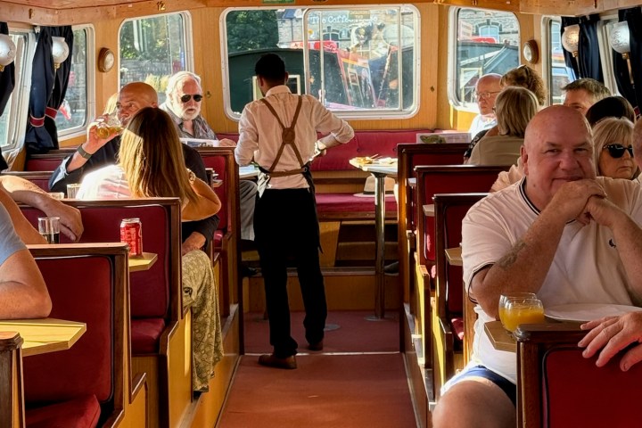 People sitting in a boat's interior with a waiter serving.