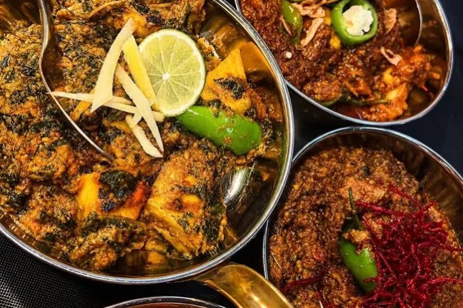 Assorted spicy dishes in metal bowls with garnishes on top.